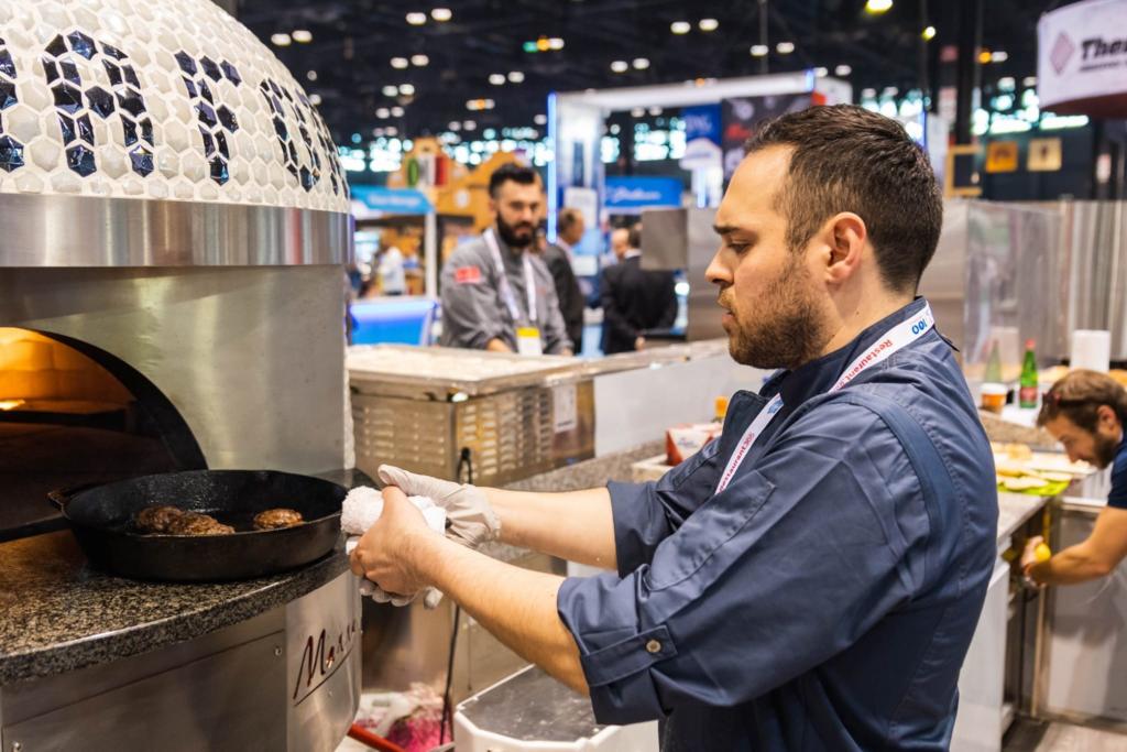 Italian Chef removes burger patties from skillet in white Marra Forni oven at National Restaurant Show 2019