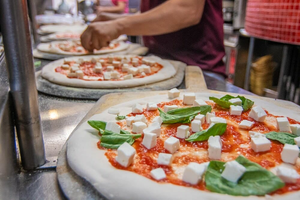 Pizza Dough being topped with tomato sauce and mozzarella