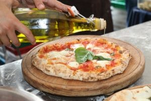 Hand Pours extra virgin olive oil on freshly baked margherita pizza