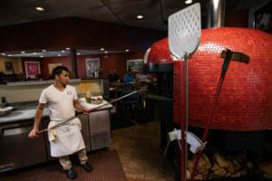 La Posta Restaurant Indoors with Chef Baking Pizza In Wood Fired Red Tiled Brick Oven