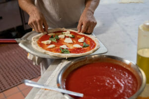 Chef Prepares to bake Margherita Pizza with tomato sauce, and mozzarella