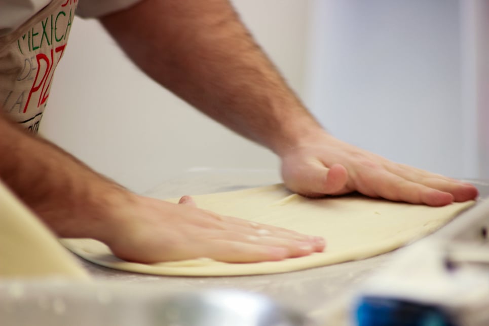 Chef flattens out dough for pizza