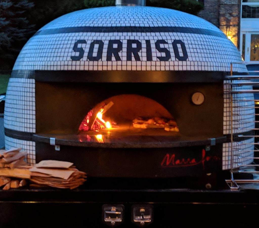 Sorriso white and black tiled brick oven at night with fire burnign inside