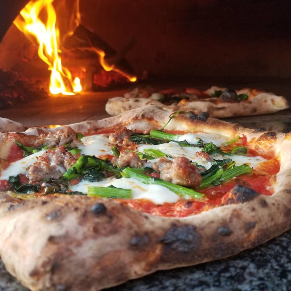 Fresh pizza with mozzarella, greens and meats in wood fire brick oven